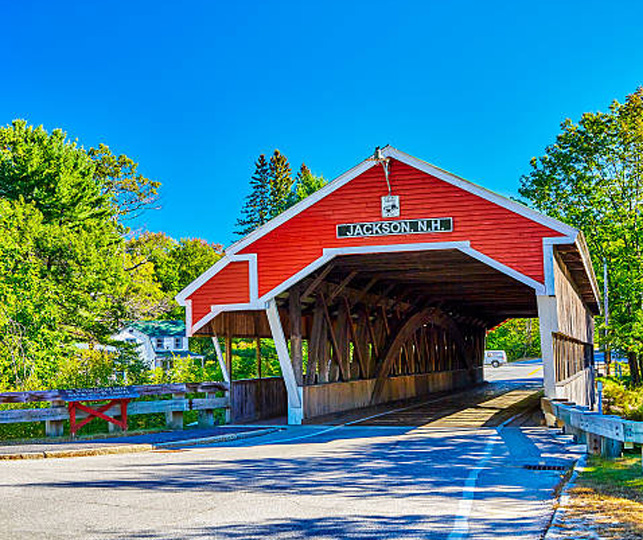 View of the Jackson, New Hampshire covered bridge. Blue skys and green trees flank the bridge.